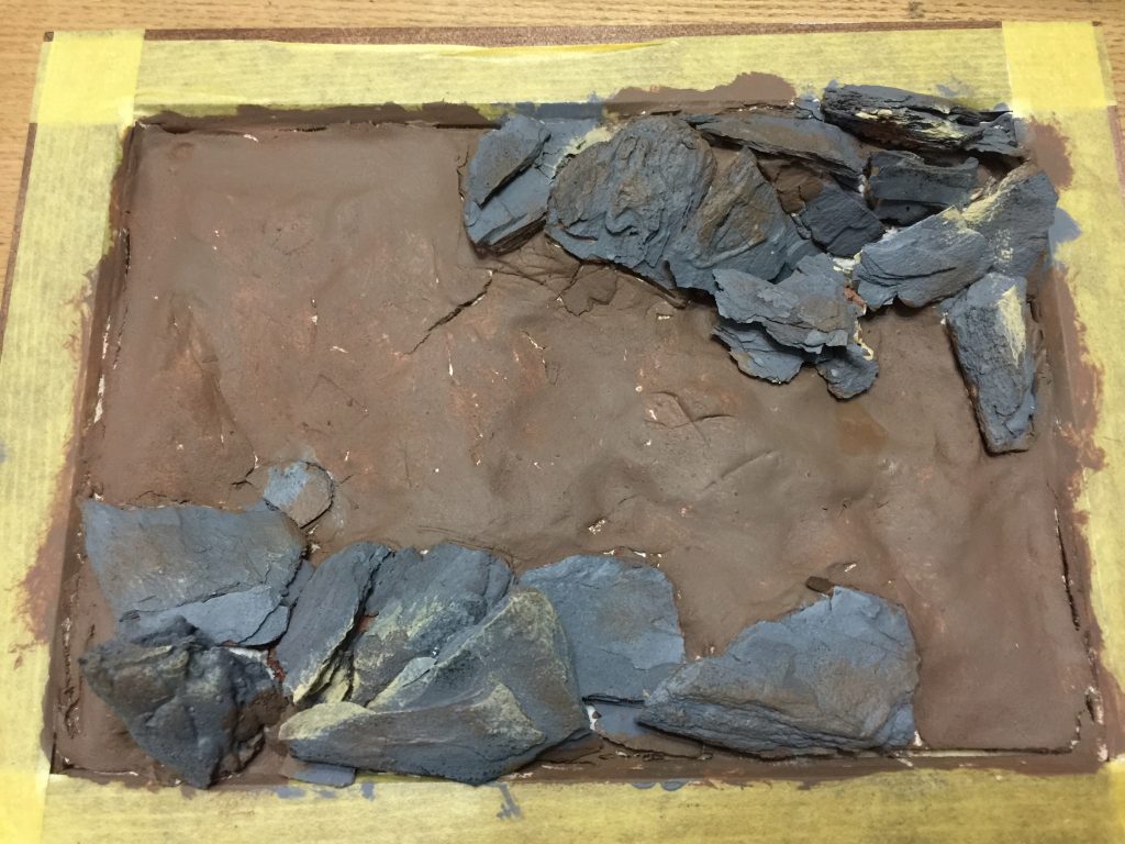 写真たてに紙粘土を敷き詰めて乾燥後ブラウンで適当に下塗りの木のチップを適当な大きさに手で割ってグレーで筆塗り後、適当に敷き詰めてボンドで接着。