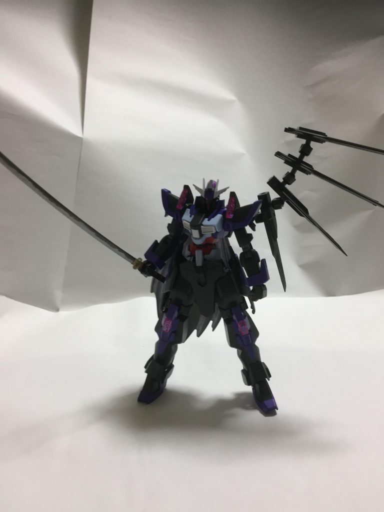 形式番号 NK-13JR
全高 20.0m
重量 80.1t
手持ちの刀は次元覇王流拳法を繰り出す時には邪魔になるが、それを差し引いても余りあるほどの強さを示す。
理由としては粒子切れを起こすことなく常にバーニングバースト状態でいられるようになったことによる恩恵である。そのため、バトル開始と同時にディナイアルガンダム・リユニオンは常に髪の毛のような粒子帯を発動する。ディナイアルガンダムの前身となったガンプラでなしえなかったこと、メイジンのみがなしえたことを出来るようなったことの証左である。フィールドを構成する粒子を自在に操ったカテドラルの能力を応用しバトルフィールドから常に大過剰の粒子を供給させ続けることに成功したのである。その制御はジュン兄の技量でも難しかったため、左に片翼状のバインダーを増設、時に翼のように、時は背部バスターキャノンとして機能しつつも供給される粒子の制御装置になっている。そして大過剰の粒子を刀に乗せることで、刀の間合いの外にあったとしても斬撃を防御不能の攻撃として敵に与えることができる。その斬撃はバトルフィールドのオブジェクトを易々と切断し、試しバトルのデンドロビウムの砲塔を竹輪の如く輪切りにしたほど。当初、この斬撃に使っている粒子を次元覇王流拳法の強化に用いていた、確かに一撃一撃の威力は桁外れに上昇し、バトルフィールドを抉る、粉砕するなどの超常的な攻撃が繰り出せていたものの、どのような粒子制御を行ってもガンプラに帰ってくる反動が異常な値になってしまい、一回一回のバトルが長引けば長引くほどガンプラ自身が耐えきれないことが予想に難くなかったために刀という外部武器に粒子を回すことで、この問題点を解決している。もし、刀が破壊されたとしても柄の部分さえ残っていれば粒子を纏わせることである程度は刀の機能を有したまま戦えるが、威力は当然劣る。
そして、刀が完全に破壊され柄も残らない時に、このガンプラは次元覇王流拳法によって戦うことになる。これこそがジュン兄の最強戦術であり、このガンプラの最高戦術である。
供給され続ける莫大な量の粒子を常にフィールドに撒き続けることで機体の耐久限度を超えないように調節するが、この時に放出される莫大な量の粒子は海流の如き暴流であり相手の機体制御を奪うことになる。その上でジュン兄が次元覇王流を用いるが、もし一撃が相手ガンプラに当たろうものなら粉微塵に吹き飛ぶだろう。無論、技が掠るだけでも全壊、ないし半壊するため次元覇王流が文字通りの一撃必殺となる。ただ、よほど注意しないと仲間が巻き添え食らう。