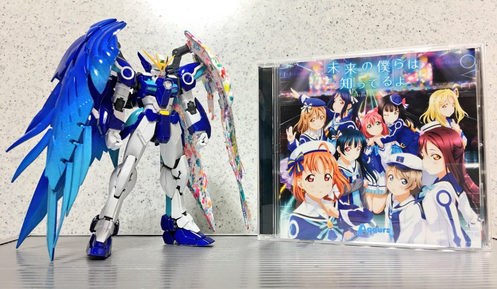 (   。・v・。)ﾉ 今回はアニメの劇中歌らもヒントをとり、カラーモチーフとした作品です。キャンバスには「0（ゼロ）から１へ」「Aqoursを象徴する青い羽根」などから、ウイングガンダムゼロ（EW版）を選びました。
ボディは主に千歌の衣装から配色しています。
物語が進むうちに取り入れたい要素も増え、どのようにまとめるかが課題でした。