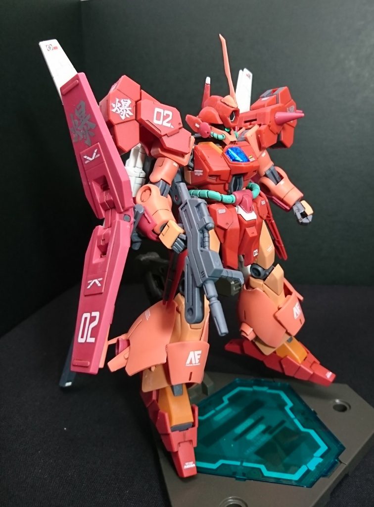 横から
今回苦労したのは顔の移植。
ジェガンの顔部分を削り取り、切り取ったマラサイの顔パーツを移植しています。
パイプを切ったので、それを隠すためにマラサイの丸いバルカン部分をほっぺたにしています。
「爆」のマーキングはブラストの意味「爆発」を、「02」はユッキーの「2機体目」とビルドダイバーズの「2番機」を由来としています。