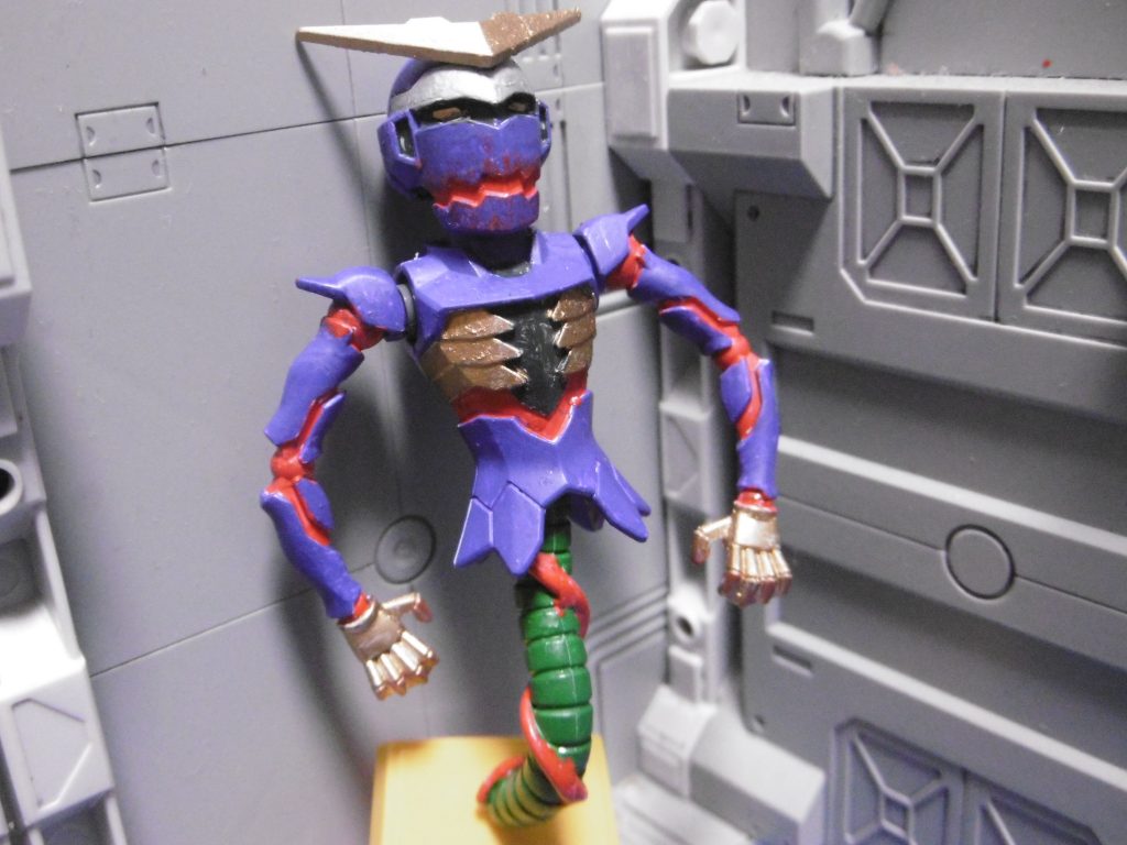 『呪いの根源』は、HGガンダムジエンドの イッカク。名前は最後まで決まらず、通称のままになっています。
元々は白一色だった彼を、8色で塗り分けしました。
筆が難しかった箇所は爪楊枝で塗ってます。
写真では青系の色に見えますが、実際には紫(クレオスのパープル)。
使っているLED照明の都合、そう見えているだけです。
根?の配色はすぐに決まり、最初見た時からナメック星人の腕かと思った。口の周りと指先はブラッドレッドで軽くドライブラシ。
【ドライブラシ】は、通常はモールドの強調や汚しの技法なようですが、城スケールモデルでは石垣の表現(石垣には様々な種類の石が使われている)によく使うので、それを用いてみました。自分のやり方で合っているかは分かりませんが、仮に正しくなくても自身のやり易いように最適化させています。個人的には「ランダム性がある塗装による面の強調」目的で使う事が多いです。
本体を石垣に見立てた理由は、ボール本体正面のモールドがそれっぽく見えたから。モールド追加しようかと思ったけど、逆に汚くなりそうで却下。
亡婁は、主に城の廃墟をイメージした妖怪のハズでした。
しかし完成したモノはご覧の有様。寧ろ良くなった感も。