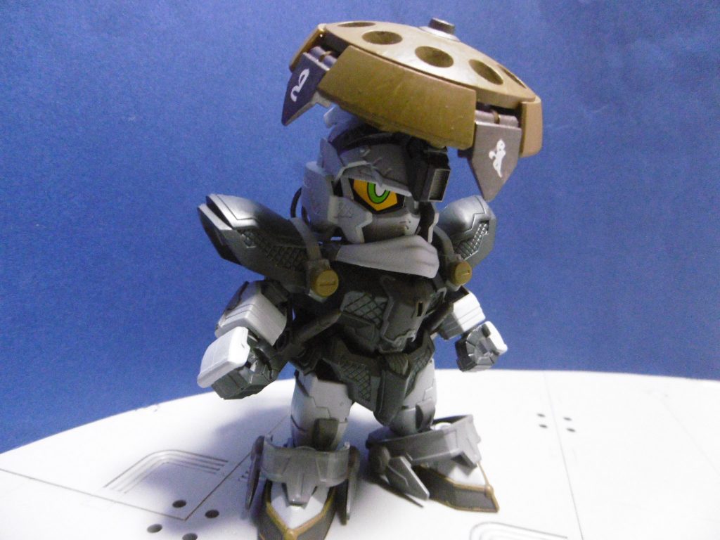 僧イメージで笠を装備。増設ジョイントでＨＧＢＦ Ｒ・ギャギャのシールドと３ｍｍ接続。重い装備のため、ジム顔を付けると重心が後ろになり自立が難しめ。笠が無ければジム顔でも普通に立てます。
頭頂部は対空機銃を仕込み、笠周囲の穴には道具を隠し持ちます。焙烙玉・煙玉・各種材料など様々。放下を披露する際の道具を入れたりも。

ただの仕込み笠ではなく四天王の守護を受けており、正面が北方。印を結ぶと特殊障壁の効果を発動し、梵字が出現（発動させない限り普段は見えず普通の笠）。各９０度前方＆上方からの全属性ダメージを８割減（※半減と書いていましたが誤記。厭戦的＆静的重視のため防御を強固にしています）。
ただしデメリットもあり、累積ダメージによっては破壊される可能性。決して無敵ではありません。
防御機能を切れば、各方角の射出口（元キットでビーム刃が出る所。守護障壁はココから発生）より小型の投擲武器を放つ事も出来ますが、障壁に比べて使うメリットは殆どありません。

マフラーは首元のみ。マフラーは近現代的な忍者の記号でもありますが、その用途ではなく「顔の一部」です。僧兵の顔を覆う袈裟みたいな類で、色を頭と合わせているのは一目で忍者と分からないように。