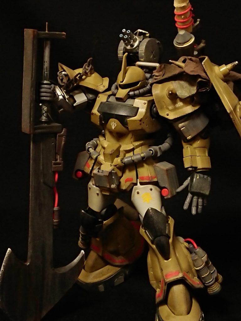 ジオン残党軍の戦闘狂パイロットが駆るグフタイプのモビルスーツ。高出力カスタマイズを受け、試作機のパーツも多数使用。ケンプファーを参考にした強襲能力を獲得しており、高い瞬発力を活かして得意な接近戦に持ち込む。残党と協力関係にあるゲリラからは、現地の神話に伝わるとされる怪物「鎧蠍」の異名で呼ばれており、その名がそのまま連邦軍駐屯部隊からの本機の呼称として用いられている。調査に向かった調査部隊や威力偵察用のms部隊がことごとく行方不明になっており、本機と抗戦、破壊されたと思われる。