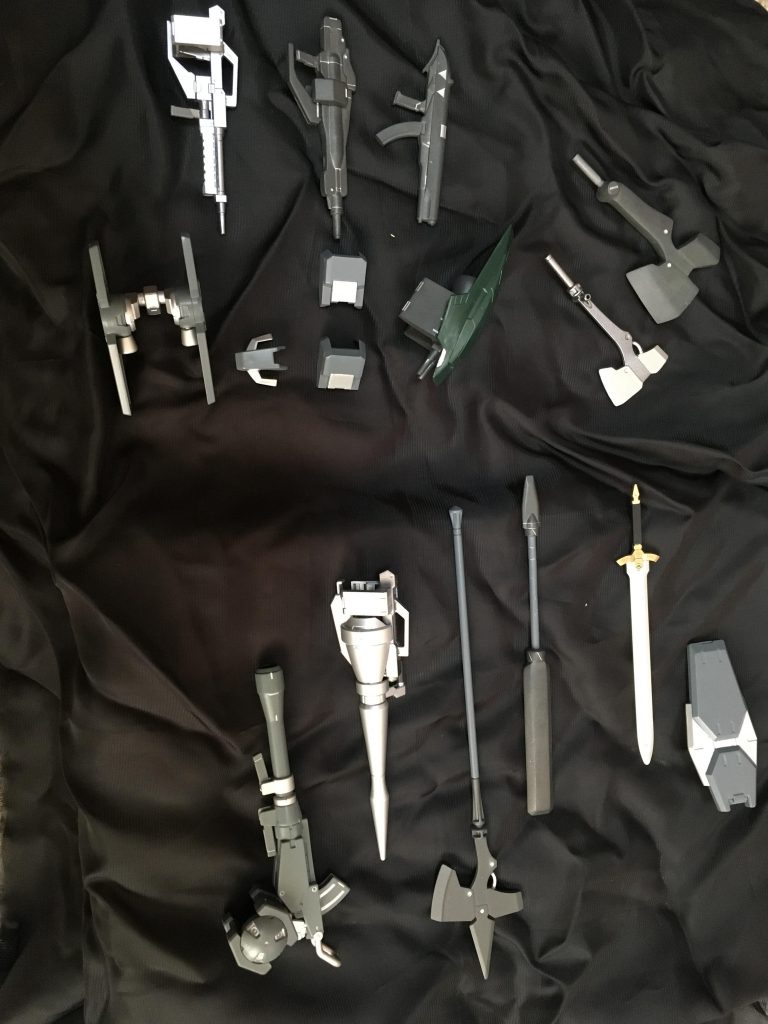 装備や予備パーツ一式。右上に先程のアックスがあります。これは通常グレイズのアックスを三枚重ねて、あとはパテで刃渡りを大きくしたもの。だいたい5倍くらい重たいけれど磁石固定部分にはネオジム磁石を2つ使っているため、難なく装備できます。その左のモノは、バーニア付二連ライフル付バックラーを作ろうとして大きすぎることに気付いたものです。装備を作る時は大きさも気にしなきゃダメですね…。その下にあるパルチザンは、パテで重量を増した獅電のもの。他装備は、合わせ目処理と塗装をした程度のものです。