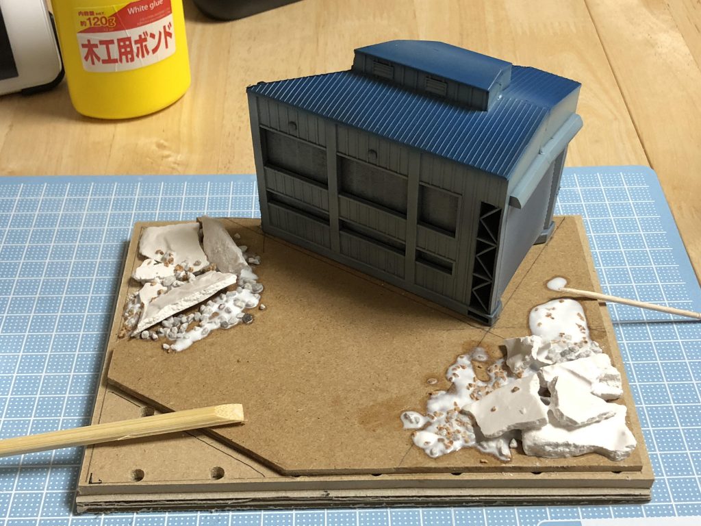 100均素材でお手軽に台座を製作中。地面はMDFとダンボール、瓦礫は石膏とコルク、建物は鉄道のおもちゃ。まだ取り付けていないけれど、草はグリーンシート、外枠はフォトフレームを使って。1000円以内で作れる!