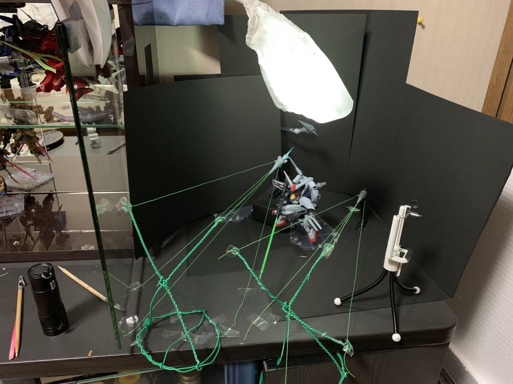 これがドラグーンエフェクト撮影の全貌だ‼️
ビームの正体は蛍光グリーンで染め上げた縫い糸でした。アクリジョン蛍光カラー、ブラックライトでよく光ります😎
糸だから、引っ張ってテンションをかけてあげない弛んでしまいます。右の糸を引っ張ると左がたるんでしまったりで、バランスをとるのがとても難しい😓
プロヴィデンスのドラグーンは大型ドラグーン3機にそれぞれ9門、小型ドラグーン8機にそれぞれ2門で、合計43門ものビーム砲があるのですが、流石にこの仕組みでやるのは無理なので大型ドラグーン2機にそれぞれ5本、計10本のビームにしておきました。
10本だけでもセッティングがひじょーに面倒臭く二度とやらないと思います😵