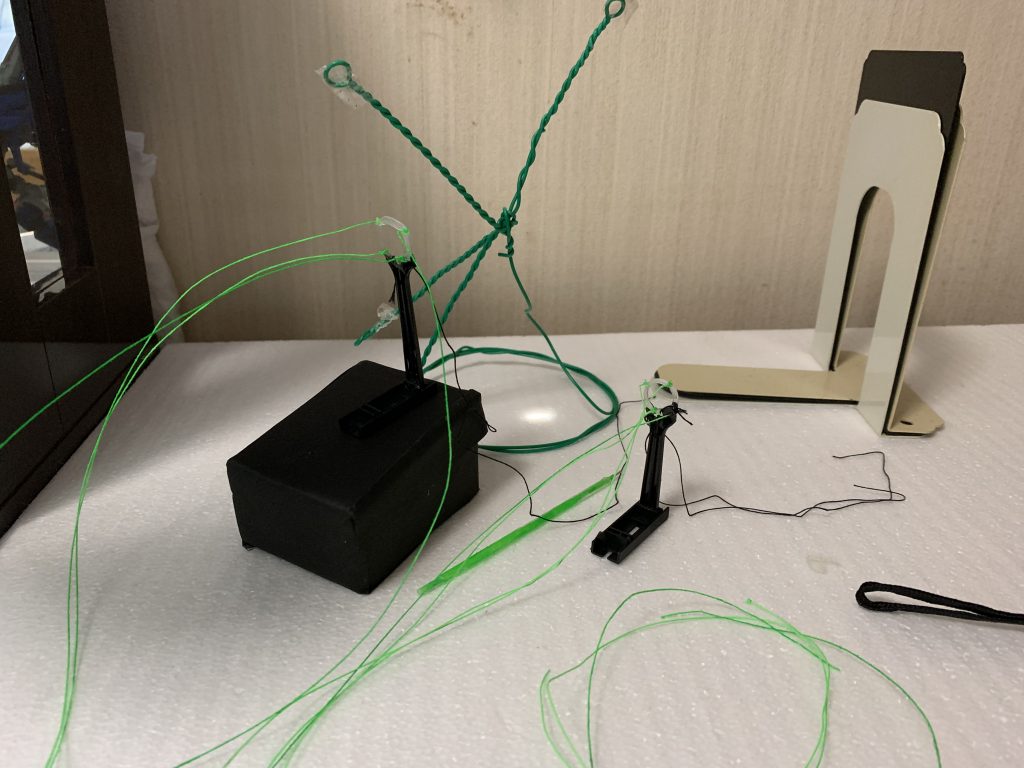 ドラグーン用小道具について追記します。
バラして明るいところで撮るとこんな感じです。
ドラグーンを支える支柱は百均のかき氷用プラスプーン製です。中央にドリルで穴を開け、さらにテーパーリーマーでドラグーンが入る大きさまで穴を広げました。
目立たないように黒く塗ってあります。前方からの引っ張りに耐えられるように後方に黒い糸を張って釣り合うようにしています。
ビーム糸は結びつけてから瞬着で結び目を固めています。
左側の黒い物体は発泡スチロールを適当に切り出して、背景と同じ黒画用紙を貼ったものです。左右で段差をつけるために使いました。
後ろにある緑の変な物体は、上に向かってビーム糸を張るための針金で適当に作ったアームです。
ビームライフル用エフェクトは、外径2mmのクリアプラ棒と外径3mm内径2mmのクリアプラパイプとUVレジンで作りました。
プラ棒を蛍光グリーンで塗る→プラパイプの中にUVレジンを注入→さらにその中にプラ棒を挿入(なるべく気泡が入らないように注意)→UVレジンを硬化させる
という手順です。屈折率の関係で全体が色付きのクリアパーツのように見えます。今回は気泡が入りまくりましたが 😓
