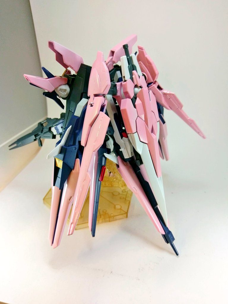 この形態は「ダブルオーサクラ・春疾風(はるはやて)」になります。ペタルにちょっと装備を追加しています。
GNドライブをもう一基、そこにセブンソードのバスターソード、サイドに1.5ガンダムのウイングバインダーを追加しています。ウイングバインダーを追加することで機動性を上げ、バスターソードとGNドライブでGNフィールドを展開することができます。もちろん大剣として使用できますが、GNフィールドや盾としての役割が強いです。
ダブルオーサクラ・ペタルは集団戦を想定したHWSですが、防御力と継戦能力に懸念があり、それを克服するためにGNドライブを追加してGNフィールドが使えるようにした、という設定です。
背面だけですが段々とピンク色が多くなってきましたね!