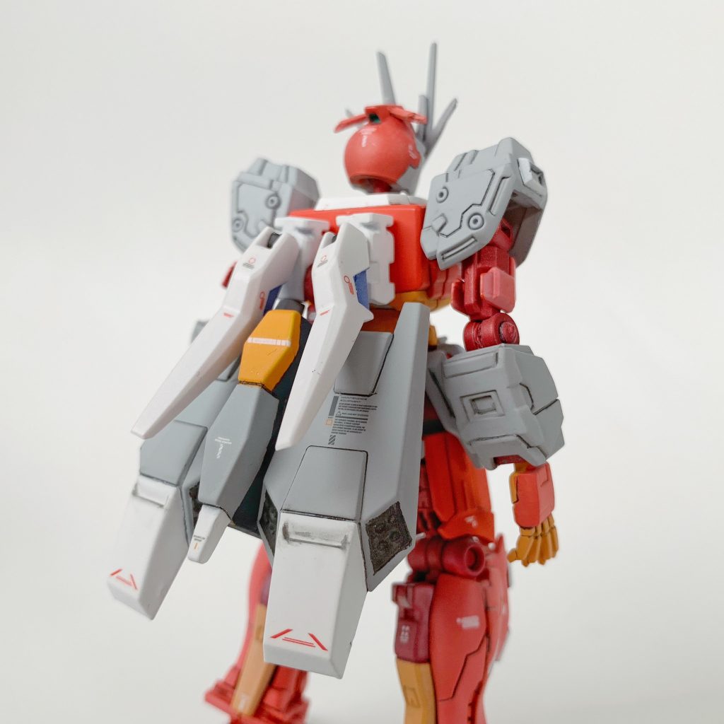 ナラティブ B装備の有線式遠隔攻撃端末とバックパックは、独自解釈μガンダム化のとき同様に思い切ってカットし、小型シールドや切断した固定フレームを組み合わせてリビルド。前述のように、G-アルケイン以前に建造された試作機という脳内設定に基づき、スカート型スラスターの試作品のような装備と位置付けています。バックパック接続位置の穴が目立ったので、ユニコーン ペルフェクティビリティ化(1体目)の作業中断で保管してあった後ろ脛のスラスターカバーを固定フレームの接続部ごと移植して目隠ししました。ちなみに、リギルド・センチュリーの世界ではビーナス・グロゥブ以外は「ファンネル」の開発・実装をしていない(G-アルケイン フルドレスの独立可動式レーザービーム砲は、ビーナス・グロゥブで入手した資材を用いて製作した)ようだったので、今回は有線式遠隔攻撃端末部分(ファンネルもどきとケーブル格納部)はオミットしています。