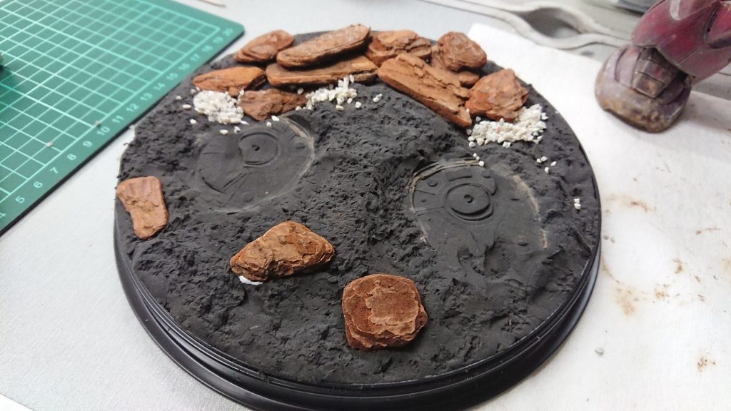 台座は100均の蕎麦の皿を裏返しにして、その上に黒い紙粘土でベースとしました。
茶色いのはバークチップ?みたいな物で岩にしようとしています。
白いのも観葉植物用かな?細かい石のようなやつです。
すべて100均素材です。