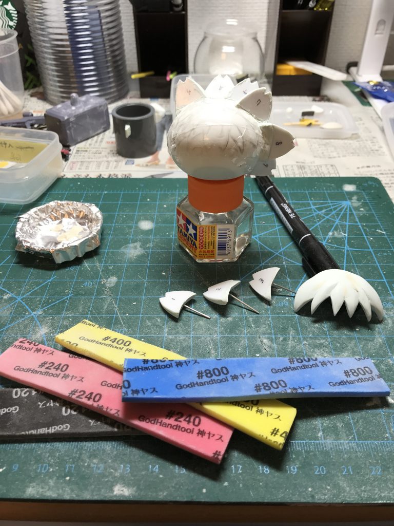 最難関の髪の毛です。
前髪はデコ部分だけぐらいで作り、その他の髪の毛は1mmのプラ板2枚でエポキシパテをサンドイッチ。
そのエポキシパテ部分に1mmの針金を刺して成形。
あとは頭の取り付け部分にドリルで1mmの穴を開けて差し込み。
頭は曲面なので密着するようにその部分にもエポキシパテ盛って、外して成形して、そのパーツを付けてチェックを延々繰り返す...。
それを16パーツ...。