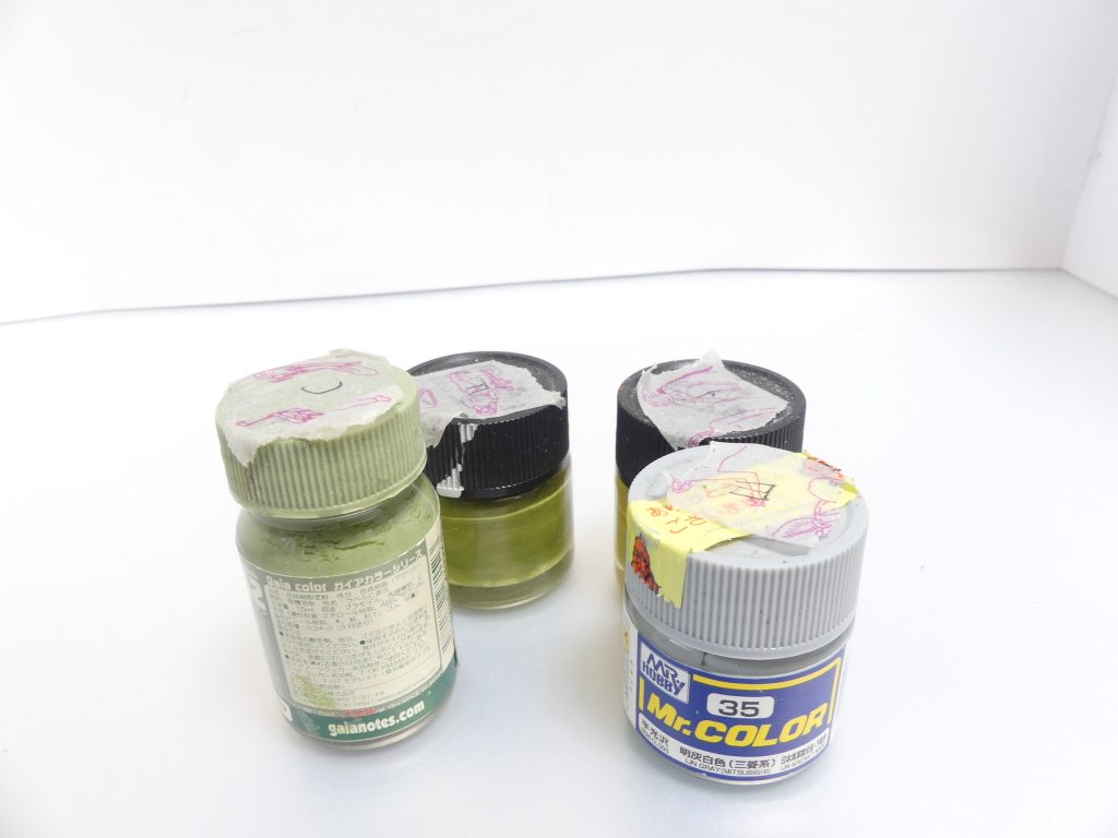 ロ「まず塗料！
筆者はラッカー塗料メインだ。住環境の関係でスプレーを使うには模型製作スペースに行く必要があるが、夏にはそんな暇などなかったので全て家の中で完結させている。
ガイアノーツさんのプレミアムマットパウダーは必須だな。
前編でも触れたように、RGは細かい色の変化が特徴的なシリーズだ。アニメとは異なり、「PS装甲の電圧が云々」など様々な理由で、同じ色に見える装甲がパネルごとに分かれている。
筆者は今回、パーツごとに筆塗りすることになるし、一日にかけられる時間の関係上長期にわたる戦いとなるので･･･忘れないように各色の上にマステでランナー文字を書いておいた」