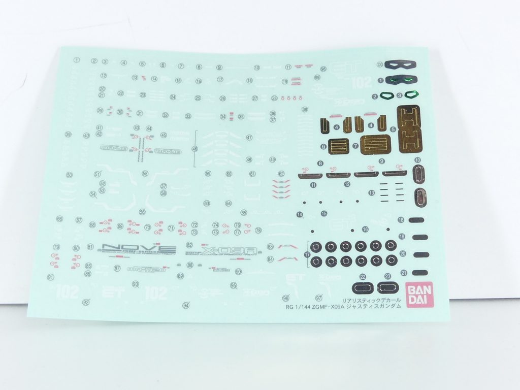ロ「*リアリスティックデカール*！
デカールと名前が付いているがシールだ。あくまで*「現実考証の末とてつもなく細かくなったマーキングシール」*と考えていただきたい。
RGのシリーズが進むたびに少なくなっていくように感じられるが、このジャスティスは初期RGなので総計150枚ほどある（一部は選択式）。
自分のスキルやキットの調子などに合わせ使い分けたいところだな。
なお、他キットに対しても当然ながら優れたマーキングシール代わりとなる。[アルザスのGNヴィンテージ](https://gumpla.jp/hg/153585)あたりを例に取ってみようか。

特殊印刷により金属表現を楽しめるのも特徴･･･となっているが、塗装する場合仕上げ的に「浮く」事もあるので十分注意だ。トップコートなど、お好みの方法で調整をかけても良かろう。
また、上級者は別売りのガンダムデカール（商品有無はキットによります）を使ってみよう」