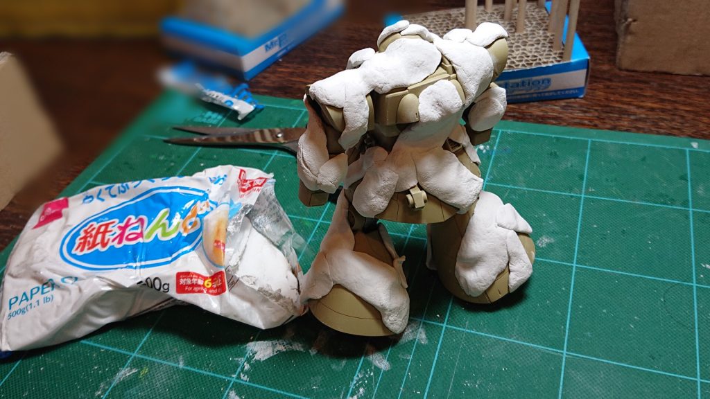 最初、紙ねんどをちぎっては張り付けるうちは、
「結構やり易いし、余裕ジャン!紙ねんどチョイス、yeah!」
とか思ってました。
ちなみに、ベース色は
タミヤラッカーのLP-55ダークイエロー2を吹いてます。
紙ねんどマスキングをした後、いよいよ茶色を吹こうとしてドムを持ち上げた瞬間!
バラバラっと紙ねんどが剥がれました…
おそらく、紙ねんどが乾いたので粘着力が無くなって表面に張り付いていられなくなったのでしょう。
それに、紙ねんどの成分が影響しているのか、ベース塗装がひび割れました。
今回、サフレスでベースを塗っているとはいえ、塗装が割れるのは紙ねんどが乾燥すするときに収縮した影響かもしれません。
とりあえず気を取り直して、もう一度紙ねんどマスキングをやり直して茶色を吹きましたが、塗装中に紙ねんどがどんどん乾いていき、剥がれまくりです。
結論。紙ねんどはマスキングに向きません。まぁ、DAISO製品が駄目なのかもしれませんが。
仕方なく急遽、フリーハンドで迷彩を書き入れます。と言っても、我が家のエアブラシは