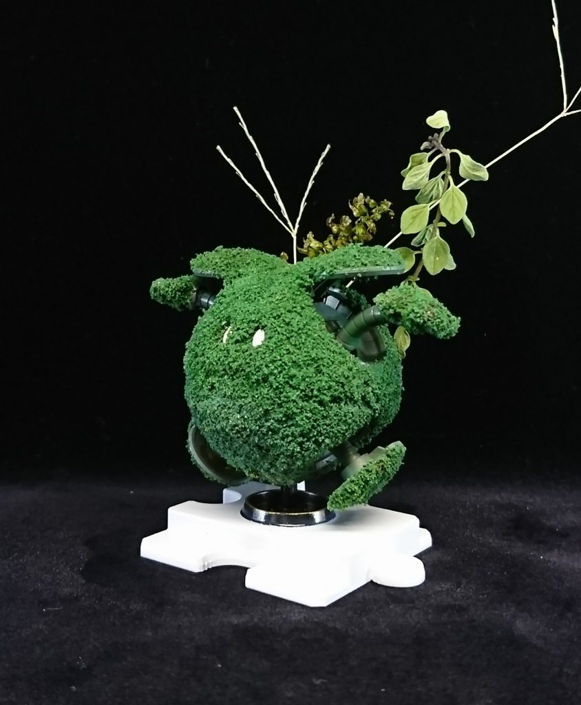 苔玉ハロのアップ。全体にアクリジョンのベースグレーを吹いた後、外装部分にジオラマに使うグリーンの情景素材をまぶしました。ハロの口元がほんのり残るようにまぶし具合を調節しています。また、所々にクリアオレンジやクリアイエローを垂らし、色合いが微妙に変わった箇所を作っています。
