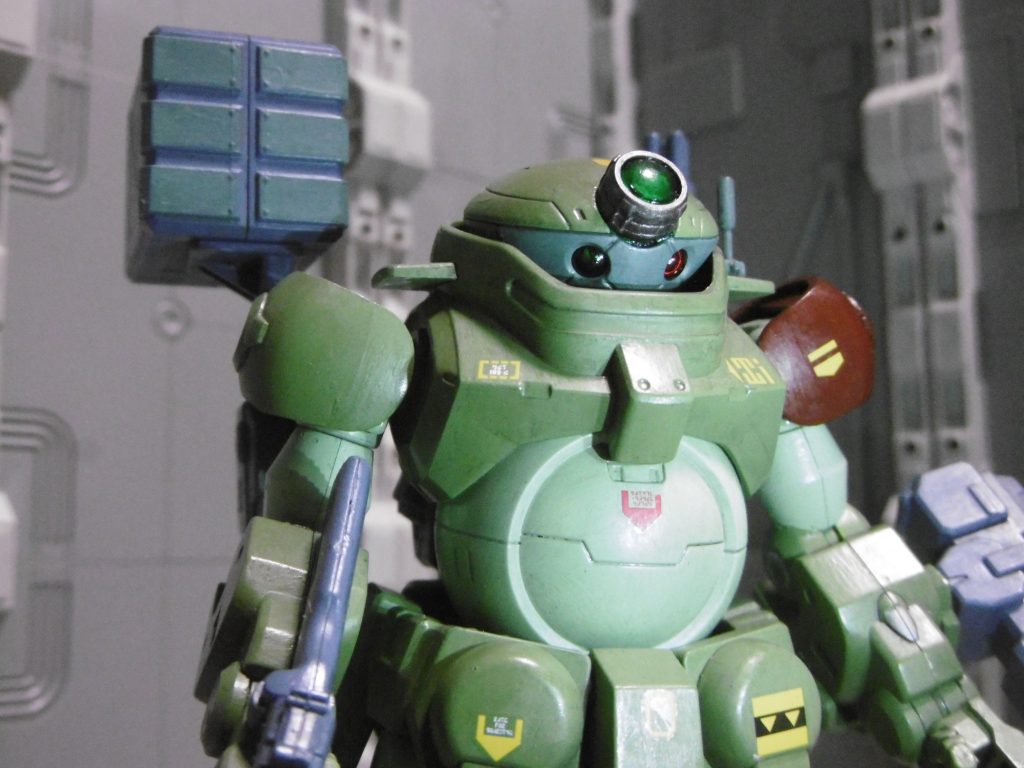 頭部もスコープドッグ風の配色に。
中央レンズは、同系のＭＳサイトレンズ０１を前後貼り合わせ。すると片側が窪むのでクリアーパーツを覆うように接着固定できます。
サイトレンズはピンクしか持っていないため、クリアーの同径Ｈ－アイズに変えて接着。クリアーグリーンで後から塗っています。この要素は後から急遽追加しました（本当は前作のグリモアで使うはずだった）。