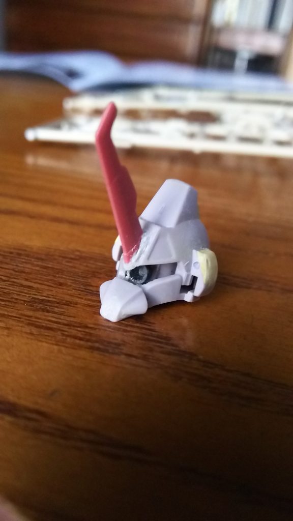 それからトサカと登頂部を削ったり耳にパテを盛り穴を空けバルカンポットにみたててみたり、モノアイの十文字が気に入らなかったので変わりにギラ･ズールのバックパック横のちっこいバーニアを仕込み緑のレンズと一緒に接着。