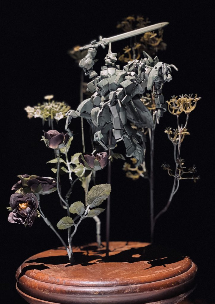 死にゆくカルタを見守る最後のシーンでありながら、キマリスの手にはグレイズリッターの剣が持たれており、お姫様を守る騎士のよう。花々に囲まれたその様子はもしかしたらカルタの夢の中なのかもしれない、現実と虚構の間の雰囲気を目指して作っています。鉄の華とはまた違った、夢想の華のような気高さと儚さがテーマです。