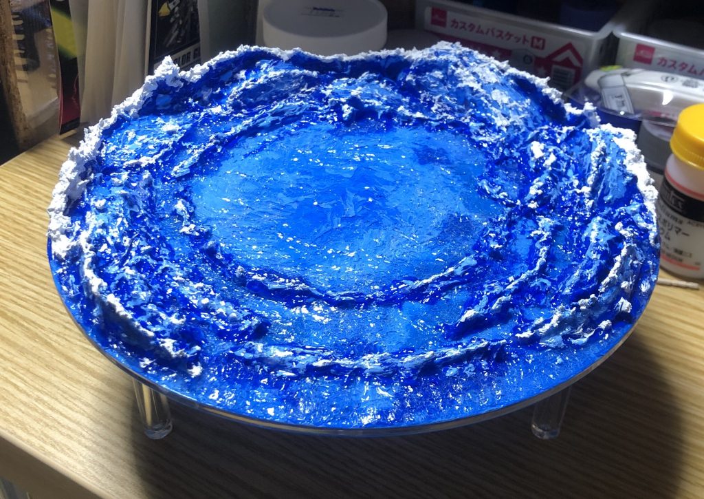 凪の台座製作。
初めて使う素材、水の表現も初めてなので悪戦苦闘しながらの製作でした。乾燥に時間がかかるので製作にも日数を要しました。
台座はセリアのディスプレイスタンドを使用。モデリングペーストとカットしたクリアファイルで大きな起伏を作り、その上からスーパーヘビージェルメディウムと青い絵の具を混ぜたものを塗って波を表現。その上に水泡表現素材を混ぜたもので白い波しぶきを追加しています。
