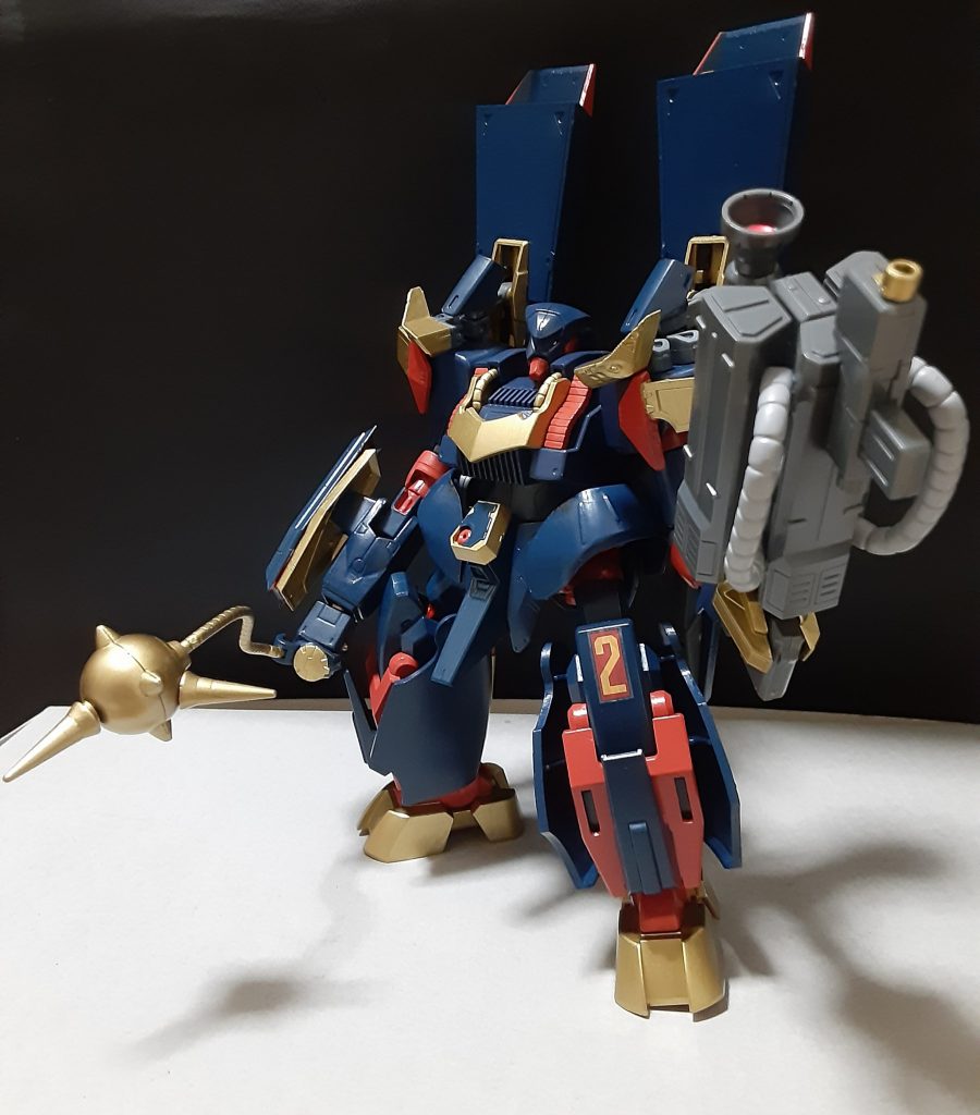 機体名:ダ・ンバ

[武装]ゴールドハンマーウィップ、ウェポンアームB型、バインダー内蔵ビームキャノン、となっている。

[総合スペック]1.0~13.0の内。
8.5と想定。

張りぼてに見える姿とは裏腹に優れた耐久性と高い推力を持った機体。
左腕には固定された射撃武器ウェポンアームB型が装備されている(A~Iまでが開発されているとされる)。