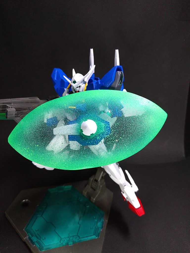 GNビームシールド「ビーム」の名が付いているが実際はGNフィールドを板状に展開したもの。
ガンダム00版ビームシールドです。エクシアのGNソードのシールドの青い部分を短くカット。中央に3mm穴を開けて、リペアIIのブースト状態のGNドライヴ先端部分を軸を2mmほど延長して接続しました。ビームエフェクトは100均の透明プラ板を楕円に切って作りました。ガンダムマーカーのメタグリーン→蛍光グリーン→メタグリーン順でエアブラシシステムで塗装。最後にプレミアムトップコート光沢を塗布しました。