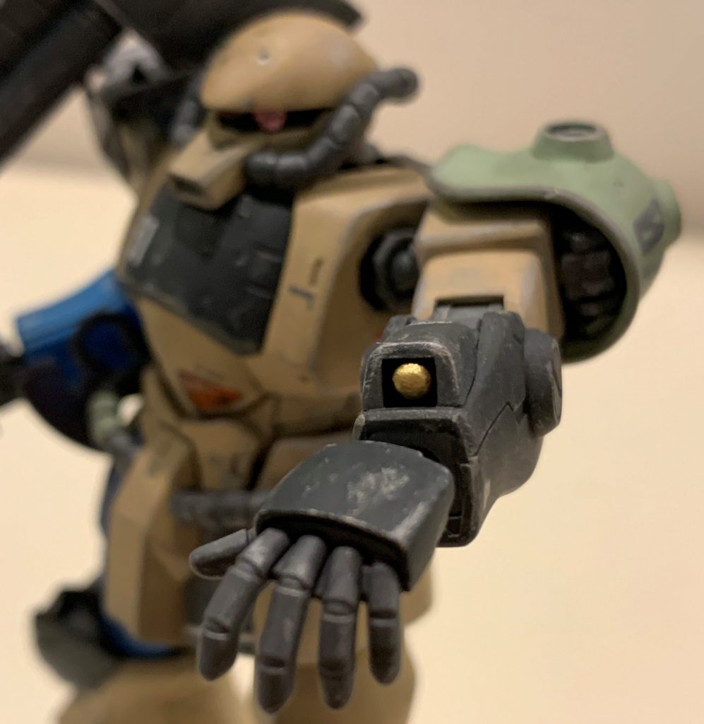 補給されたB型の前腕ヒートロッド射出機構を改造し、MMP-78と同じ弾を撃つグレネードランチャーにしているという、オラ感丸出しの設定です。ヒートロッドや指バルカンの弾倉が内蔵されていた訳ですから、グフの前腕内部は結構な空きスペースがあると想像し、このアイデアに行き着きました。通常この機構が付いているのは右腕ですが、射撃武器を持つと使いづらいのでこのグフは左手に設置しています。構造上装弾数は減りますが、スモーク弾、閃光弾、HEAT弾、榴弾など、場面に応じて弾種が選べるよう内部は分割式弾倉になっている、という設定です。見えている弾頭はランナーの先を丸めて塗ったもので、穴内部で接着しました。 +