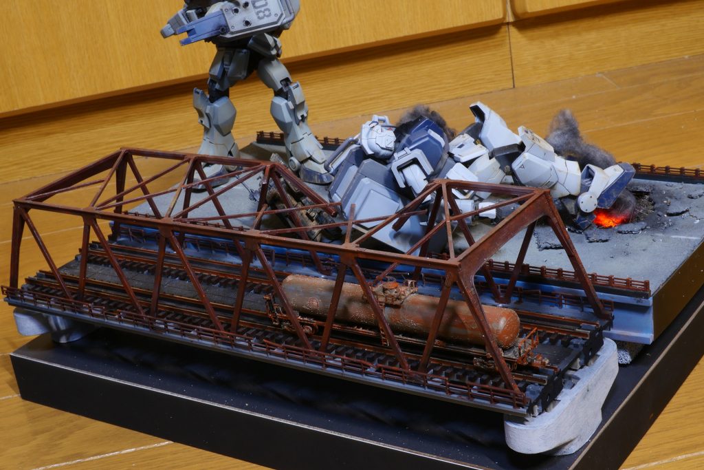 鉄橋部分はNゲージのストラクチャをほぼそのまま流用して、経年劣化で錆びが回ったように表現してみました。また、劇中には無いですが、陸戦型ガンダムを倒れ込ませて破壊されたように工作しています。