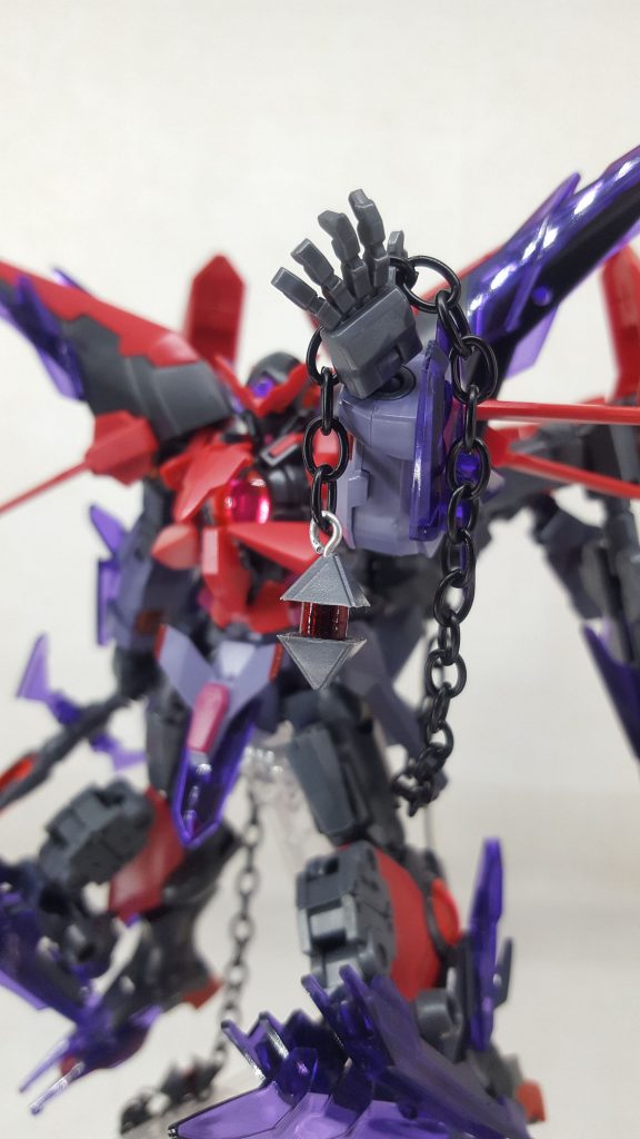 武装5【GNチャーム】「呪いは恐怖ではない。真に恐れるべきは、呪いを宿すに至ったその身の業である。救った人々の、仲間の、愛する人の声が・・・己の正義を苛む呪歌に聞こえ始めた」機体に繋がる鎖の、その先端にある装飾具です。これこそ、当機体の中で最も畏怖すべき兵装になります。この兵装は動力炉に内臓されたサイコフレームと同質の素材で作られており、リバース・サイコ・ドライブが放出する負のエネルギーと共鳴して機体周囲に負のエネルギーフィールドを展開します。このフィールド内は負のエネルギーで満たされており、中に入ると精神に何らかの影響を受けます。例えば、妙にイライラし始めたり、悲しくて涙が止まらなくなったり、怖くて震えが止まらなくなったり・・・最初のうちは大した影響は受けません。ですが・・・負のエネルギーの浸食量が多くなると、徐々にその感情を、自我を抑えることができなくなっていきます。人によっては、味方のちょっとした行動に苛立って暴力を振るい出したり、命令を無視して勝手な行動を取るようになります。最悪の場合、同士撃ちなどを始めてしまうことも・・・つまり・・・このフィールドは、パイロットから冷静な判断力を奪うのです。戦場において、冷静な判断が下せなくなることほど恐ろしいことは無いと考えます。間違いなく死に直結します・・・このフィールドを「MP(Mental pollution)フィールド(精神汚染フィールド)」と呼称します。MPフィールドはニュータイプのような、感受性の強い人間により強く影響を及ぼします。このような人たちは、フィールド内に侵入すると強い吐き気や目眩を起こすため、精神汚染が悪化する前に気づくことができます。そこでいち早く離脱する判断が下せなければ、どうなるかは前述の通りです。テラ・スオーノのような人を操ってしまうような力はありませんが、隣にいる仲間が徐々に狂っていく様を見るのは、まさに地獄です。尚、フィールドは時間経過と共に範囲が拡大していきます。そのため、後方にいるからといって安全では無く、司令官クラスの人物が暴走する危険もあります。また、前述のトラジック・ジェノサイダーやデストラクションバスターの負のエネルギーを高める効果もあります。