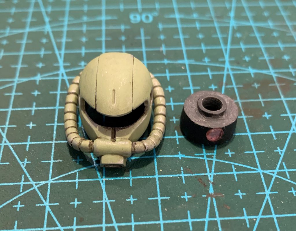 頭部は容赦のない左右モナカ構造なので、接着し合わせ目消し後、中身を全部くり抜き頭頂部に軸を付け、HGUCザクのモノアイレールを首関節で串刺しにし、頭頂部の軸に差しています。元キットに比べて首との接続位置がかなり前に移動したので、胴体側の付け根を前進させています。モノアイはピンバイスで穴を空けビルダーズパーツのMSサイトレンズを嵌め、付属シールの銀色部を裏打ちしました。