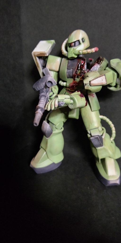 旧1/144HGザクの身体に頭は旧キット1/144ザクタンクの頭を使用、ダメージ部はノコと目立てヤスリで切り塗装後つや消しと切断面を水性カラーの黒鉄色、赤、銀、オレンジなどで筆塗り、全体的な汚しはウェザリングマスターをドライブラシのように擦りました。
