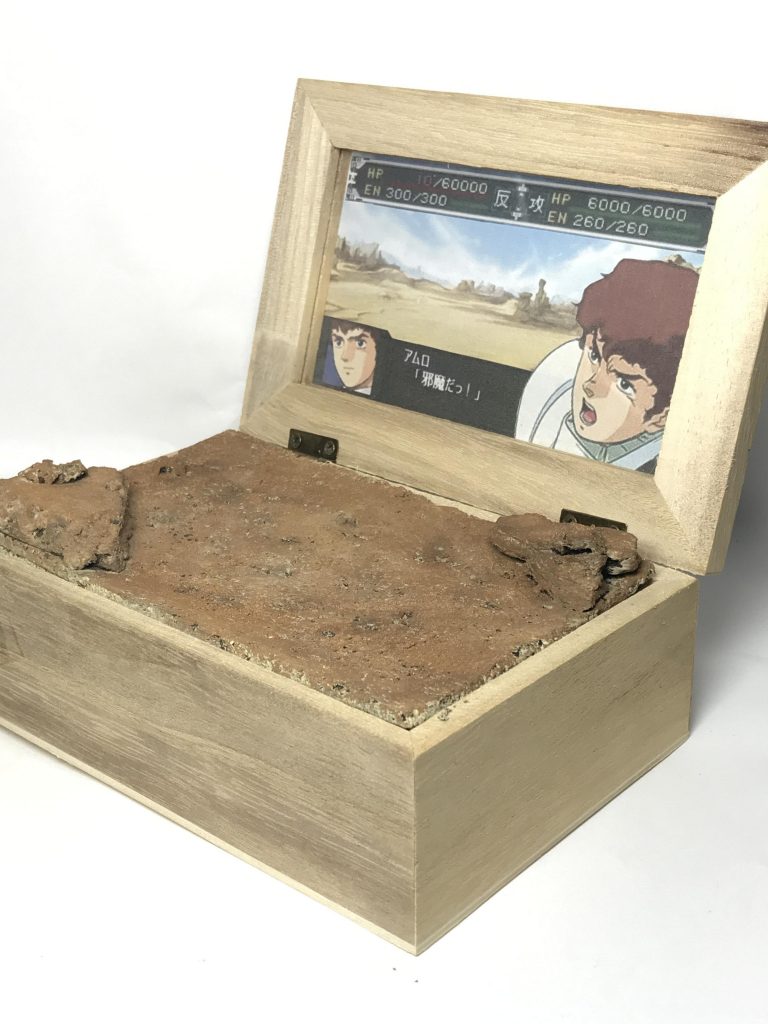 容器は100均で購入した蓋付きの木箱。地面はコルクボード、岩はウッドチップを使用。背景はいろいろなスパロボシリーズと荒野のイラストを組み合わせたオリジナルの戦闘画面です。