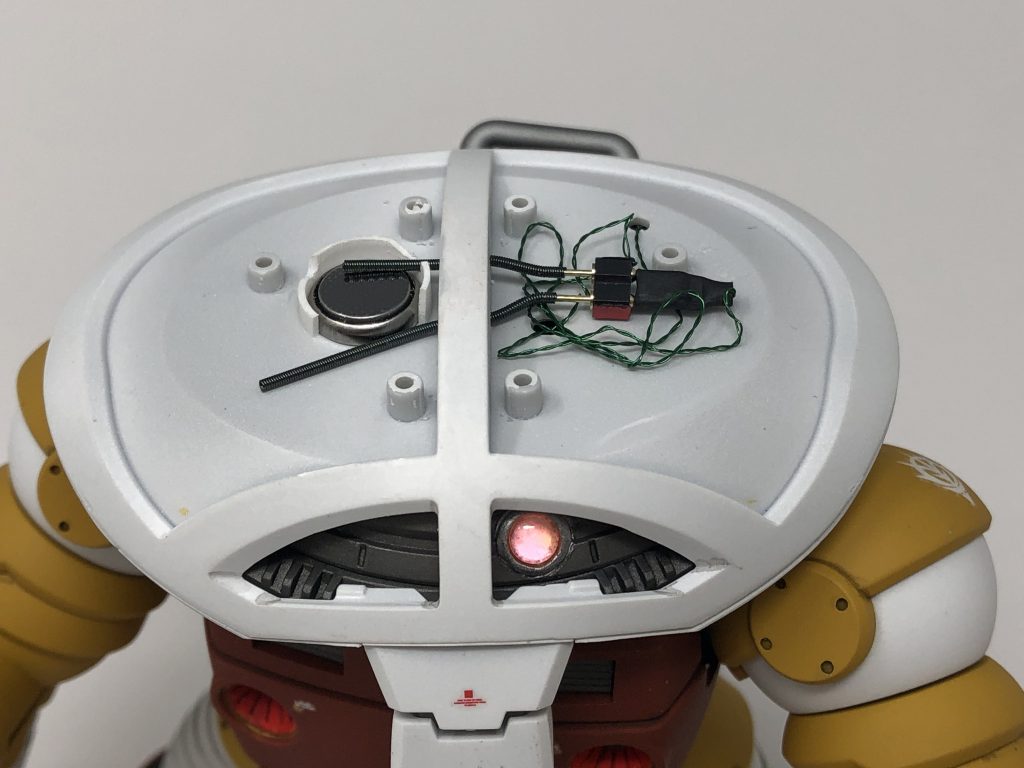 こちらが頭部装甲を外した時の状態です。頭部右側にボタン電池を配置しました。エバグリのプラパイプを加工して電池を固定しています。頭部左側からカメラアイまでLEDユニットが繋がっています。LEDユニットと電池はスプリングで接続されています。接続というよりは接触と言ったほうが正しいかもしれません。ボタン電池の電極にちょうどよく当たるように、穴を空ける位置や電池ホルダーのカット位置を調整しています。