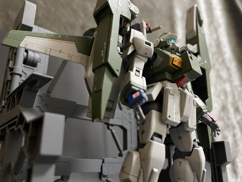 「班長！ND02、ベッドに格納完了っス！ただちに冷却作業、洗浄開始します！」「今回の哨戒任務は長旅だったからな。念入りに見てやってくれ。後ろの円盤と胸の弁当箱から情報抜き出したら管制局へ持ってってくれな」「了解です！・・・班長、この前壊れたままの右マニュピレータっスけど・・・」「そのままでいい。コイツは鉄砲握るわけじゃねぇんだ。指なんていらねぇよ。予備があるなら実戦機に使ってやれ」「嗚呼・・・。痛々しくて見てられないっスよ（涙」　胸部にはFAZZなどに使用されている追加センサーユニットを増設。班長が「弁当箱」って言ってる物です。この時代に弁当箱が存在するのか不明ですけど。　胸部排気ダクトは隠密行動用の低温化フィルターを装備。2本出ているのは固定シャフトも兼ねた排気/外気センサー。　整備員君の涙を誘う右手。前回の出撃時に破損し、そのままになっているようです。右手は銃を保持しトリガーを引く、サーベルを握るなど高トルクかつ複雑な動きをするため消耗は左手より激しいはず。実戦部隊のMSは右手予備部品がさぞ消耗しているんじゃないでしょうか。もうネモもモデル末期で予備部品の供給も滞りがち。班長の考えでは後方支援機より最前線機が優先。彩雲の右手はしばらくこのままのようです。 