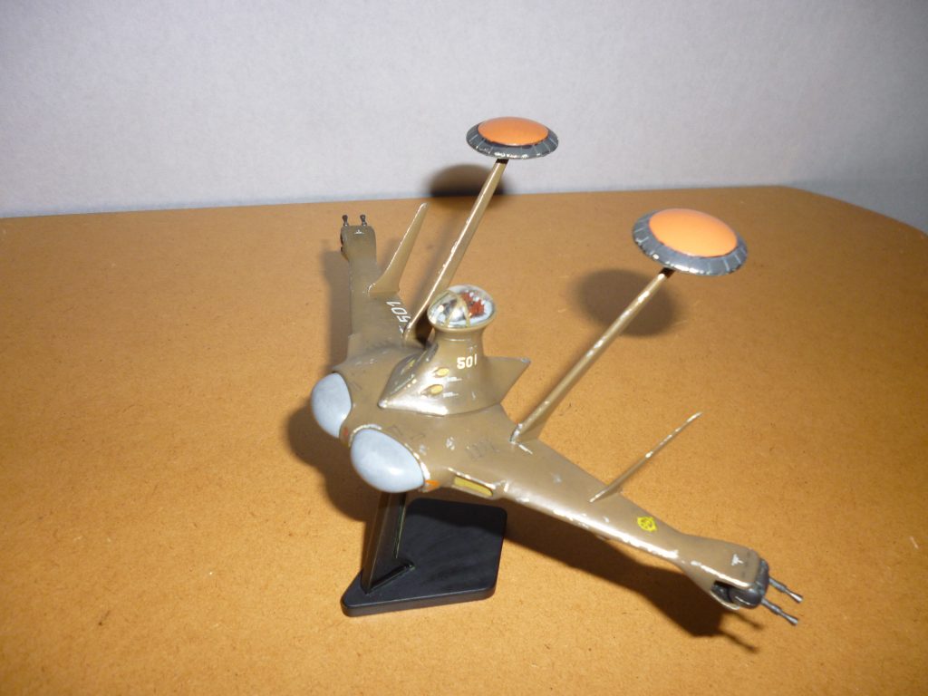 　よくある側面からのアングルです。　使用したキットは「EXモデル　1/144ルッグン」です。なぜかこのキットの成形色は緑一色だったのですが、劇中に登場した機体のイメージと合わなかったため自分で調色した色で塗りなおしました。本体はミドルストーンとオリーブドラブにレッドブラウンを少量混ぜた自作「ダークアース」です（なお、本体の塗装が終わった後で全く同じ色を模型屋で発見した模様・・・orz）。この「緑と言われれば緑にも見えるし、茶色といえば茶色だな」という微妙な色合いがかなり気に入っています(笑)。　ミサイルや排気ダクト（？）はミドルストーン、機銃は黒鉄色、機体正面のドーム状の部分（レーダー？）はニュートラルグレーです。レドームはオレンジとニュートラルグレーを混ぜた、くすんだオレンジ色で塗装しました。　これに各種マーキングを施したあと、銀色で軽くハゲチョロを入れ、黒いパステルをけずった粉を平筆で全身にまぶしてウェザリングしてあります。 