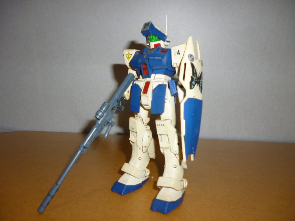 　正面素立ちです。　ベースに使用したキットは、去年のクリスマスに投稿したザク改と同じく旧キット「ポケットの中の戦争」シリーズより「ジム・コマンド」です（コロニー戦仕様のクリーム色とダークグリーンの方です）。　当時はHGUCでジム・コマンドすら発売していたか分からないような時代だったので、ベース機として使えそうなキットはこれくらいでした。　正面の改造ヵ所は・頭部バイザーをジャンクパーツとプラ板、クリアパーツのランナーで自作・右肩に取り付けるアンテナパーツを側頭部に移植（ただし１５年の間に折れてどこかへ行ってしまったので、今回の投稿に合わせてプラ版を切った端材からでっちあげ）・両胸のダクトをプラ板で塞ぐ・フロントアーマーの増加装甲（青い部分）をプラ板で製作・スネ上部のスラスター部分をプラ板で自作こんなところでしょうか。　改造ヵ所は本当に悩みながら製作しました。当時は今ほどインターネットが身近なモノではなかったので（少なくとも自分にとっては）、資料として活用できたのは本屋で立ち読みする模型雑誌ぐらいのものでした。　ちなみに、塗装はツヤ有り白とインディブルーのツートンに、ところどころ赤色です（いずれも水性ホビーカラー）。　塗装に関しても、カラーリング見本がなかなか無く、試行錯誤しました。アニメに一瞬しか登場しなかった機体で、しかも戦闘が夜のシーンだったため、当時はジム・スナイパーⅡの色は白と青のツートンだと勘違いしていました（模型雑誌でたまたま見かけた作例が「ホワイト・ディンゴ隊仕様のジム・スナイパーⅡ」だったことも大いに関係しています）・・・。それにしても、長年棚に放置してあったせいでかなり黄ばんでしまっています・・・。