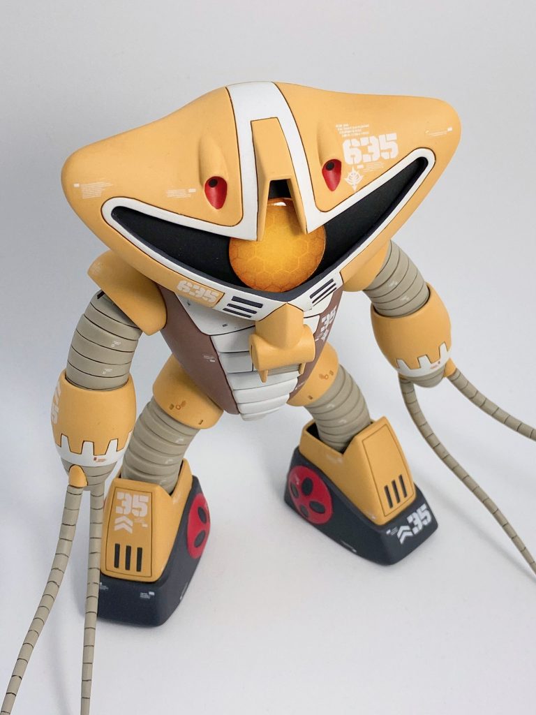 モノアイ部は丸ごと切り抜いて、裏からプラ板を貼ってモノアイレール兼 首との接続基部にしています。モノアイ本体は円形に切った透明プラ板をヤスってレンズ状に整形。高い番手のヤスリで透明度を上げ直してから、クリアースプレーでうっすらオレンジイエローに塗装。裏地にハニカム模様とグラデーションを描いた紙(Adobe Illustrator使用)を貼りました。リアル画稿や箱絵に描かれているモノアイレールのフチの黒いクマドリは、エナメル筆塗り+拭き取りで塗っています。ヒゲ状の黒やバルカン砲の赤も同様で、砲の真ん中はアーティフィシャルホール。口吻の色違いはキットだとモナカ合わせなので、モールドを彫ったプラ板を上から貼り付けました。