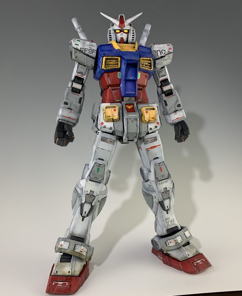 ガワラ立ち意識してポージングしました。ガンダムを作るとやりたくなっちゃいますよね（笑）目はLED発行させてもはっきりとしない印象だったので、写真映えするようにゴールドで塗装してます。HJに掲載されていた作例を参考に初めての本格的なウェザリングに挑戦してみました。 ハイライトにクリアホワイトを吹き付けて、影になる部分に暗めの色を吹いてクレオスのウェザリングカラーでピンウォッシュして立体感を狙った塗装を施しました。さらにシリコンバリアを使って、真鍮ブラシと爪楊枝とナイフで全体にチッピングを施しました。足元はクレオスのホワイトダストを全体に塗布して乾燥後にタミヤウェザリングマスターでウェザリングして使用感を演出してみました。