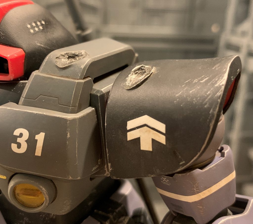 パイロットはジャブロー戦での功績を買われ、ソロモン防衛隊着任時に少尉→中尉に昇格しています。少尉→中尉は△みたいなマークが上に一個増えるだけなので、元の階級マークに加筆したという演出をしてみました。中尉のデカールを貼り全体に砂汚れを施した後、上の△マーク周りの汚れのみを綺麗に落としエナメルのホワイトで上の△マークだけ上塗りして白さを強調し、「上の△マークはソロモンで後から書き入れた」という設定を演出してみました。パイロットはどんな逆境でもしぶとく生き抜くタフガイをイメージしました。なので士官学校出のエリートではなく、下士官から叩き上げで士官になったという設定です。ジャブロー戦時は少尉でMS小隊長、新鋭機であるドムを任されていたので上官からは厚い信頼を寄せられていたのでしょう。搭乗していたパイロットを妄想すると一層思い入れが深くなりますよね。ジャブロー戦で部隊は消耗し、ソロモンに撤退後に他部隊と統合等して再編制されたと考えるのが自然なので、機体識別用ナンバーは一度上から塗りつぶし→新番号にナンバリングした演出にしようと思いましたが、うるさくなりそうなのでやめました。「設定のリアルっぽさ」と「ガンプラそのものとしてのカッコ良さ」は、必ずしも比例関係にあるとは思っていないので、適度にバランスを取るよう気を付けています。