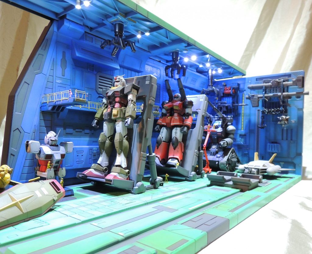 作品の全景写真です。本来、ＭＳハンガーは３台ですが、ガンダム用とガンキャノン用の２台のみ設置しました。ハンガー、ＭＳ、高所作業車、フィギュア等、全て両面テープで固定しているため、ディスプレイを自由に変えて楽しむことができます。
