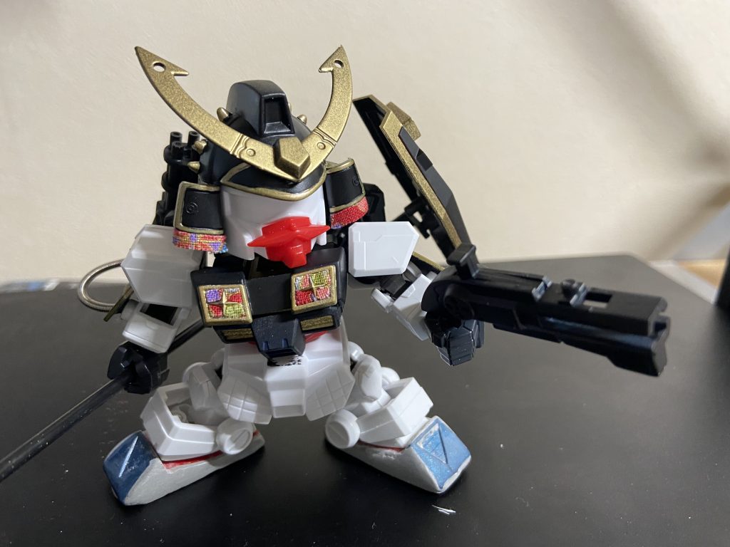 後はただひたすらに、将ガンダムの意匠をブラッシュアップしながら取り込むことに注力しました。本体‥頭部はSDフレームと接続できるように改修&前たて真ん中の五角形を大型化しました。爪先部は切り離してポン付後、パテで整形かつボリュームアップ。胸の装甲も胴体を切り刻んで別パーツ化しネオジム装着。本来肩パーツから下りてくるシールドのような意匠は、肩から下りてきているように見える位置で可動を損なわないよう腕側に接続。和柄シールをピンポイントで貼り付け。武装‥ガトリングは銃口周りのディテールアップと元ネタパーフェクトガンダムを意識してガトリングへのパイピング。盾はSDCS ガンダムから流用、スタッズシール貼り付け。手持ち銃は持ち手角度を直角から鈍角へ角度変更。槍はSDフレーム等身に合わせて長くしてます！