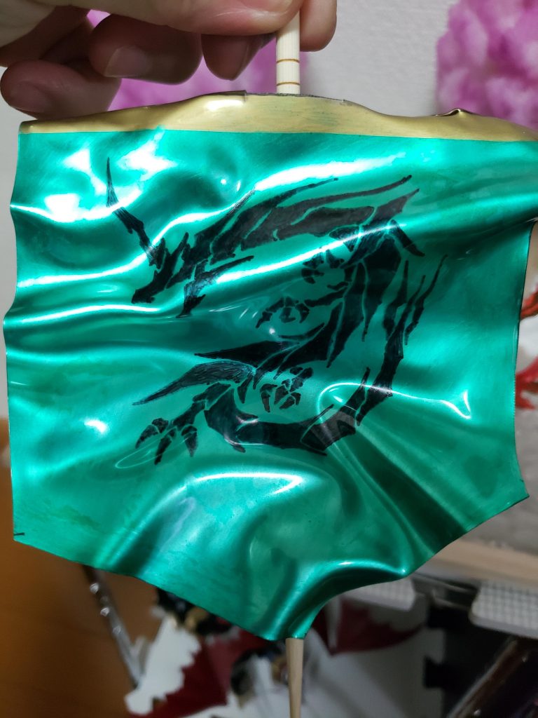 まず、エリアの旗。ネットで拾った画像を現像しプラ板に書き写しカラーリング。某ゲームでも緑をメインカラーにしているのいで、少し派手さを出す為にメタルグリーンで塗装しました。風でなびいてる様子を出す為にエンボスヒーターを使用してぐにゃぐにゃに。支柱は割りばしを十字に縛り、上部の金の部分を巻き付ける様に熱風を当てて固定してみました。