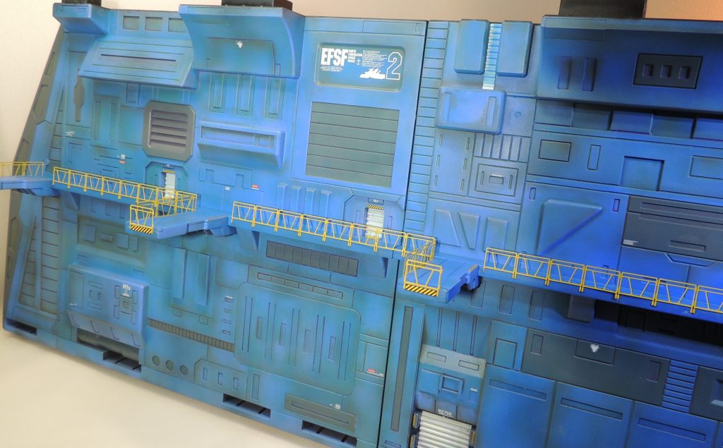 キットのキャットウォークの手すりは、太く頑丈にできており頼もしいのですが、1/144ではオーバースケールのため、「鋼魂」の薄い金属製のものに置き換えて精密感をアップさせました。壁面の塗装は、劇場版「めぐりあい宇宙」を見て、アニメのイメージを尊重し、ブルー系をグラデーション塗装しています。