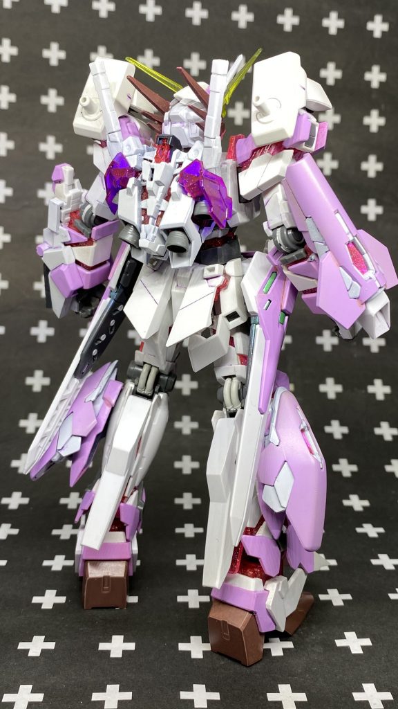 基本状態。大元のユニコーンは特に弄らずに各部位にパーツを付け足すフルアーマー方式で取り付けていきました。脚部アンクルアーマーはジャンクパーツに差し替え、ふくらはぎにはMGウイングEWのサイドアーマーに同じくMGのV2ABのヒザパーツを接着してサイコフレームを増設しました。サイドアーマーにはMGV2ABのヴェスバーを取り付け。胸部にはジャンクパーツでサイコフレームを増設を。肩部にはHGのAGE2バレットの同位置パーツを設置。右腕部にはMGV2ABのフンドシパーツにHGAGE-FXのフロントアーマーを取り付けしたものを装着。サイコフレームの制御ユニットとして取り付けしました。頭部はアンテナはユニコーンモードの角が無改造で取り付けできたので短くしたものを取り付けし、勿体ないとは思ったけど新入学だからという事で限定のユニコーンガンダムのパールクリアVer.のアンテナをサイドに取り付けし側頭部には猫のひげをイメージしてフェネクスのアンテナを取り付けました。フェイスはへの字スリットを埋めてアゴを延長して細く削り女性機体に見えるようにしました。全身のサイコフレームはパールクリアVer.のモノがピンクで鮮やかでラメが入っているのでそちらを使用しました。
