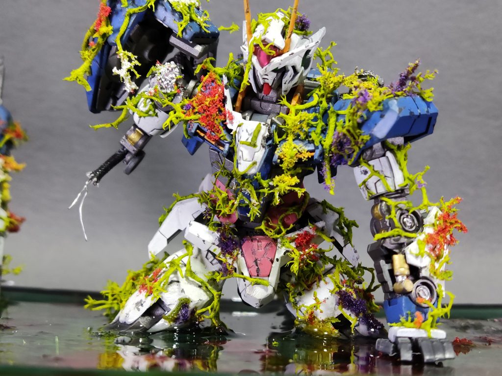 最後にギリギリまで悩んだのが「機体の状態の解釈」でした。様々な作例を拝見させていただきましたが、1番多く感じたのが「戦闘によりダメージを受け、乗り捨てられ風化と共に自然と一緒になっていく」といった表現が多く感じられました。しかし劇場版の最後のシーン、刹那が50年ぶりに愛機であるエルスクアンタと共に地球に帰還したあのシーンです。確かに地上に着陸した瞬間、機体とその周辺に華が咲き乱れていきました。ダブルオーガンダムがエンディングで華にまみれていたのはストーリーテーマを比喩した物だとばかり理解していましたがもしかしてＧＮ粒子によるものなのでは?と解釈することもできます。なのでエンディングのダブルオーガンダムが華にまみれているのは戦闘直後の可能性もあるわけです。よって私は風化したような淡い色の表現を避け、華の色味に負けない様にしっかりと機体色をアピールしていくようにしました。結果、機体の輪郭がハッキリとして華と機体の境界線を作ることができました。個人的には満足です。