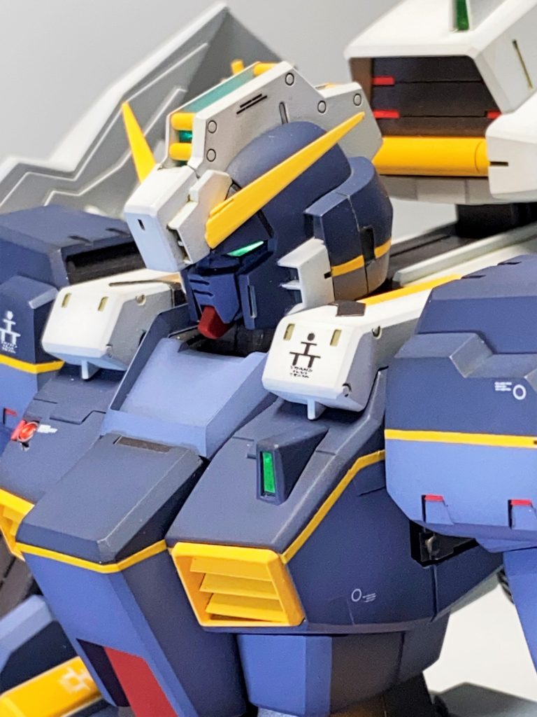 頭部の段落ちは埋め、耳部分は段落ちを残したところがポイント(作例の再現)。顎の赤パーツはやや厚みを増して角度を変更。マスクは後ハメ化も兼ねて、エポキシパテで固定しているので、キットとは取り付け位置が異なります。右胸センサーはHアイズ等から自作。胸ダクトフィンは抜きの都合で水平になっているので、プラ板で角度を変えて作り直し。全く見えませんが、肩アーマー裏モールドパーツを作って仕込んでいます。その他、作例準拠でディテールアップ。左肩エンブレムは空山氏作例では貼られていないので、貼っていません。バックパック正面のセンサーは厚みが気になったので、一旦切り離して薄々加工した後に再接着。