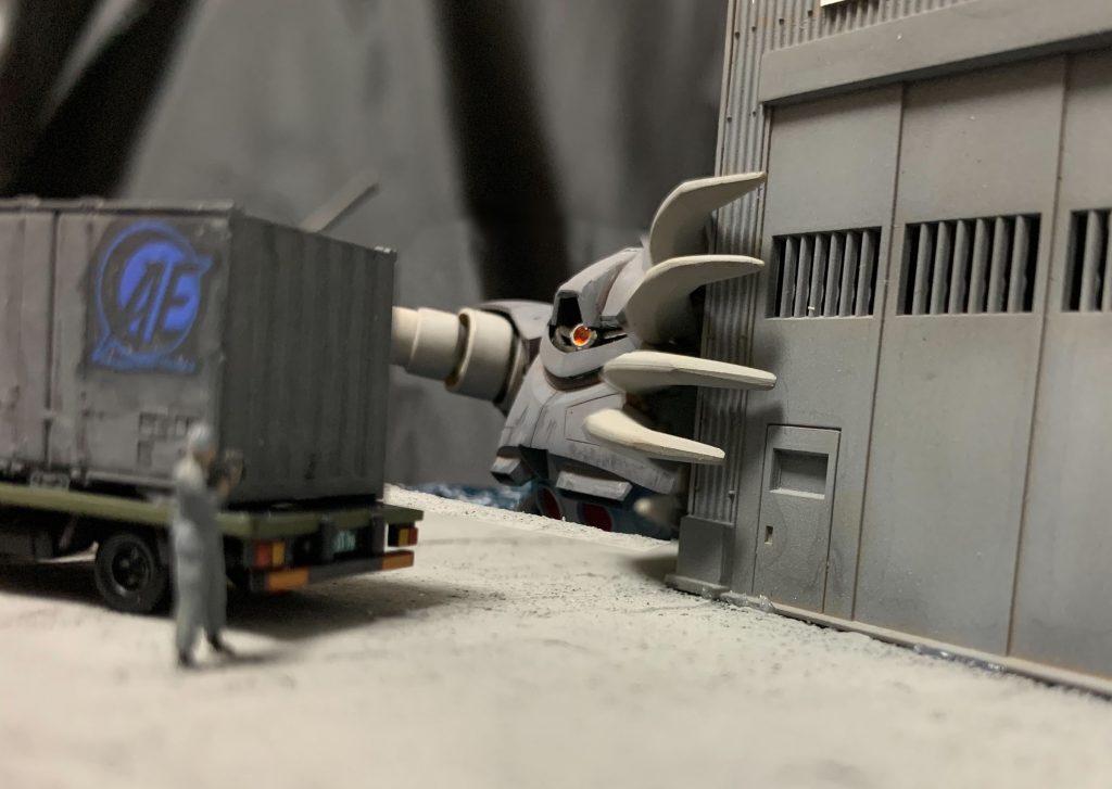 とりあえずこのショットを撮りたかったんですよね。実は配置場所に失敗して左手が建物に届かず、左右の腕で関節の数が違うのが悔やまれます。トラックの5tコンテナはNゲージ用のままだと日通の塗装になっていたのでグレー系で塗ってアナハイムのデカールを貼っておきました。トラックの後ろの兵士も地上戦セット付属の兵士を使ってます。