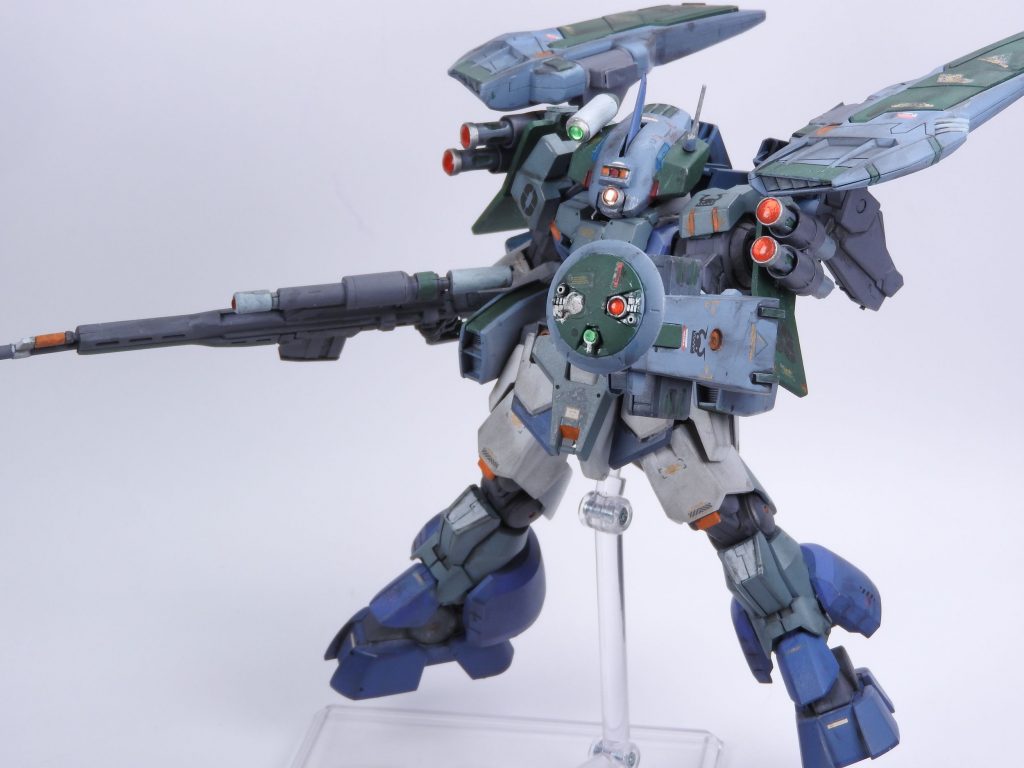 GNX-600C ゼロジンクス・サイバーアイ3番目、緑色の換装ユニットは電子戦狙撃仕様のユニットとなります。背部にはGNステルスフィールドを装備。腰部にも追加のGN粒子散布装置を装備し高濃度の粒子散布により敵部隊の目を潰しつつ、専用頭部や後述の特殊装備で強化した索敵能力により一方的に長距離から撃破する事を目的とした装備となります。両肩部にマウントした『GNサーチポッド』は本体と常にデータリンクした観測機能と通信の中継機能を持ち、高濃度の粒子ジャミング下でも味方機間のデータリンクを可能にします。左腕のデバイスは『マルチサーチャーデバイス』という索敵補助用のデバイスで、サーチポッドと合わせ高い索敵能力を機体へもたらします。