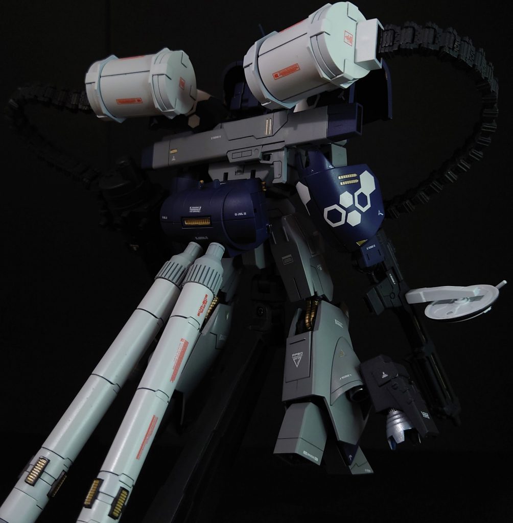 フロントショット+バックショット。武装は元々の大型ビーム・ライフルに加え、システムウェポンキット002のビーム・ライフル、MSGのガトリングガンを装着。給弾用に同じくMSGのベルトリンクを2つ取り付けて火力マシマシ殲滅仕様です。さらに強襲仕様にふさわしく、機動力を上げようとMSGのプロペラントタンクを脚部と背部に装着。MSG各種の装備は、本体に3mm軸の穴を開けて装着しています。カラーリングはGファイターのリアルタイプカラーを参考にしています。また、アッシマーのような可変機には、やっぱり迷彩だろうと、ヘックス迷彩も施してみました。もう、属性過多で胸焼けがしそうです…。その他、スジボリや部分塗装、デカールを貼ってディティールアップしています。