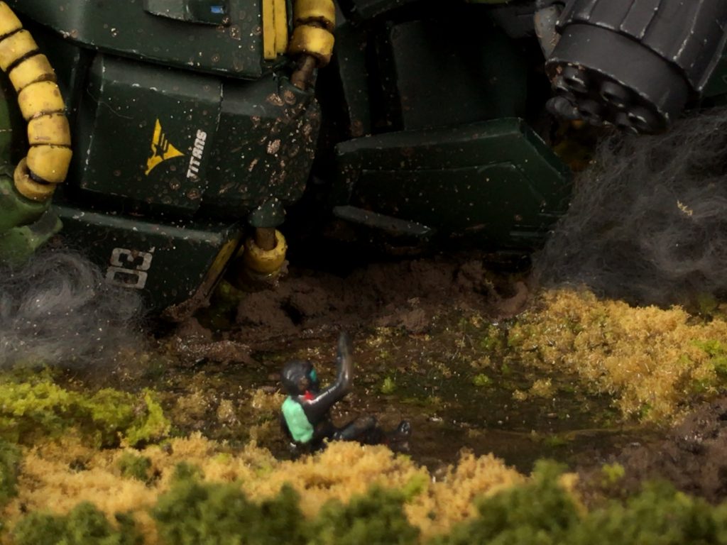 引きの写真だと見えにくいとは思うのですが被弾して倒れたハイザックから逃げ出したものの、ドミンゴに銃を突きつけられて腰を抜かして命乞いするティターンズパイロットをイメージしたフィギュアを製作して配置してます。元はビルダーズパーツのパイロットで、腕や足を切り貼りしてイメージした姿勢にして、資料を見ながらティターンズのパイロットスーツカラーに筆塗りしました。一応、腕や脚に必死に逃げ出した感を出す為に泥汚れをつけてあります。