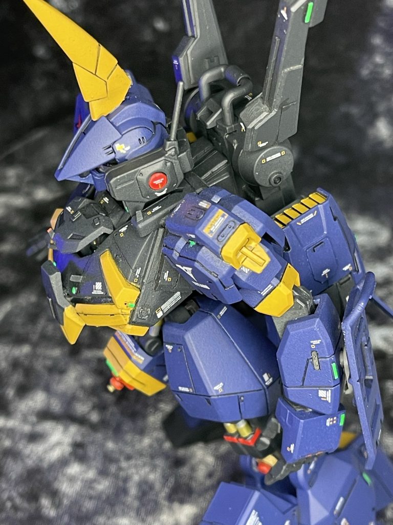 「頭部、実はほとんどがガンダムです。複雑な姿勢・出力制御をするのに電脳ユニットの容量がバーザムでは全然足らないんですよね・・・。それにツインアイ系のセンサーシステムにモノアイを接続するのは苦労しました。外殻にあわせてバルカンポッドもMK2用を使用しています。胸部はバーザムの装甲をフロート化して、ある程度実体弾への防御力もアップさせました。腕部は肩からぜんぶ、整備性を考慮してガンダム系の汎用品に変更しました。バックラーも軽量薄型にして取り回ししやすくなっていると思います。マニュピレータも本当なら汎用タイプを組みたかったのですが、重量のあるビームバスターランチャー(仮称)を保持する関係からここは大型のバーザムタイプのままです」